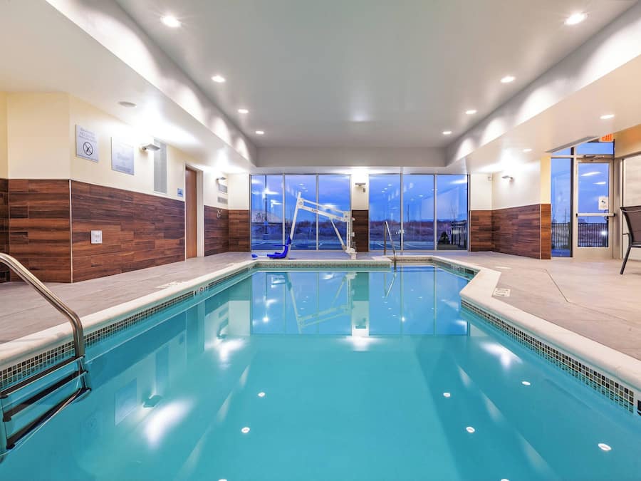 A modern indoor swimming pool with clear glass walls, wooden paneling, and a pool ladder.