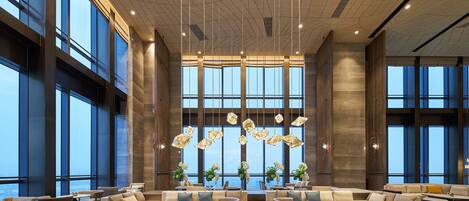A spacious lobby with large windows, modern furniture, and hanging light fixtures.