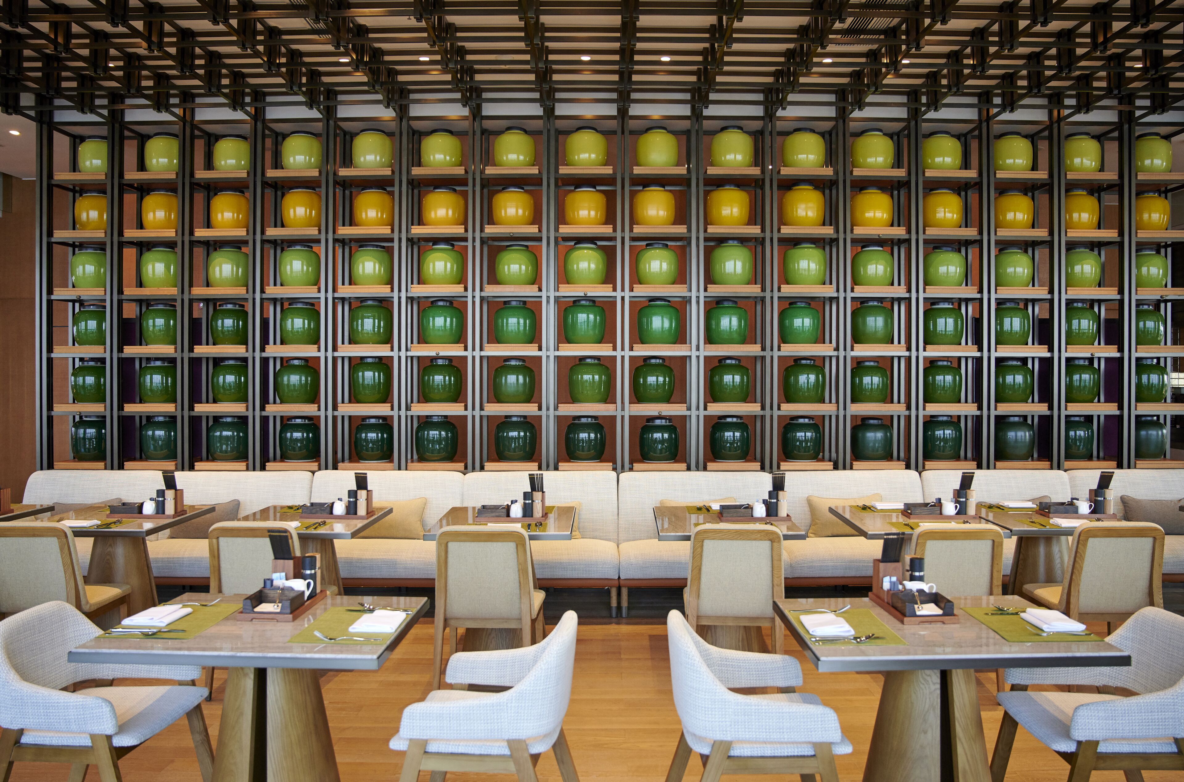 Un restaurante con varias mesas y sillas, una pared de jarrones verdes y amarillos, y un techo de madera.