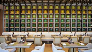 Un restaurante con varias mesas y sillas, una pared de jarrones verdes y amarillos, y un techo de madera.