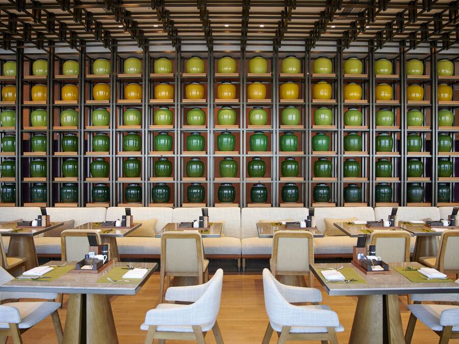 Un restaurante con varias mesas y sillas, una pared de jarrones verdes y amarillos, y un techo de madera.