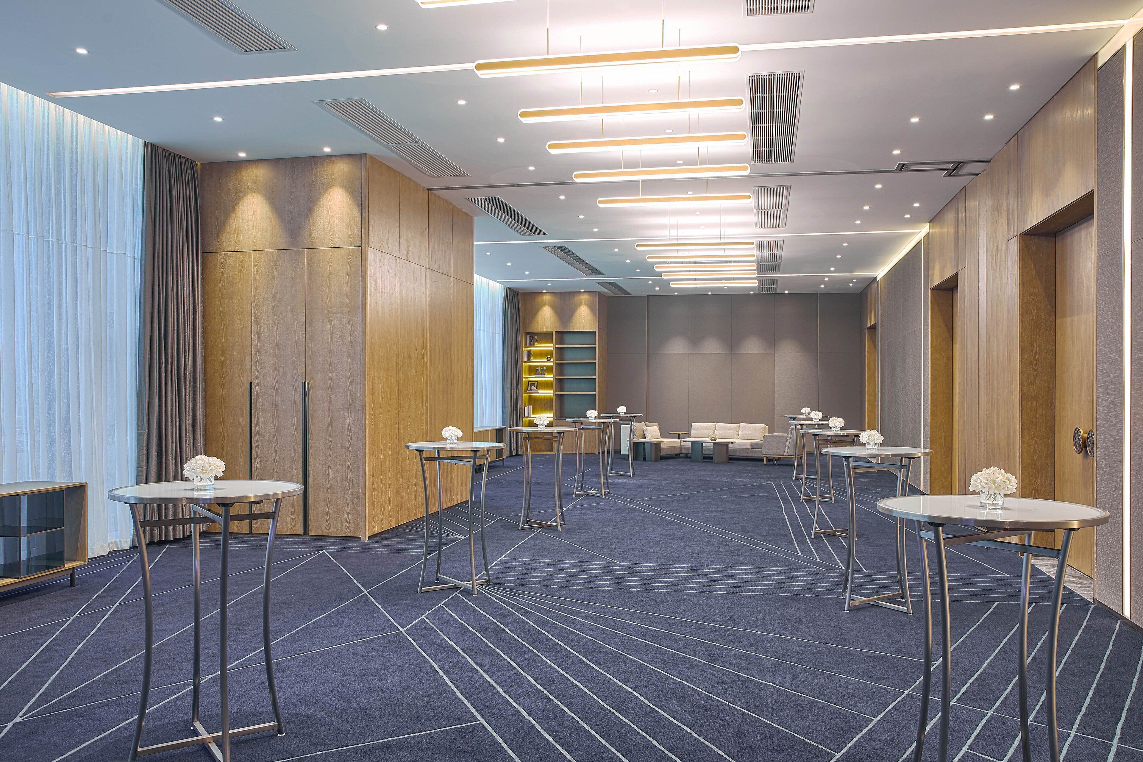 A hotel lobby with multiple tables, a seating area, and a reception desk.
