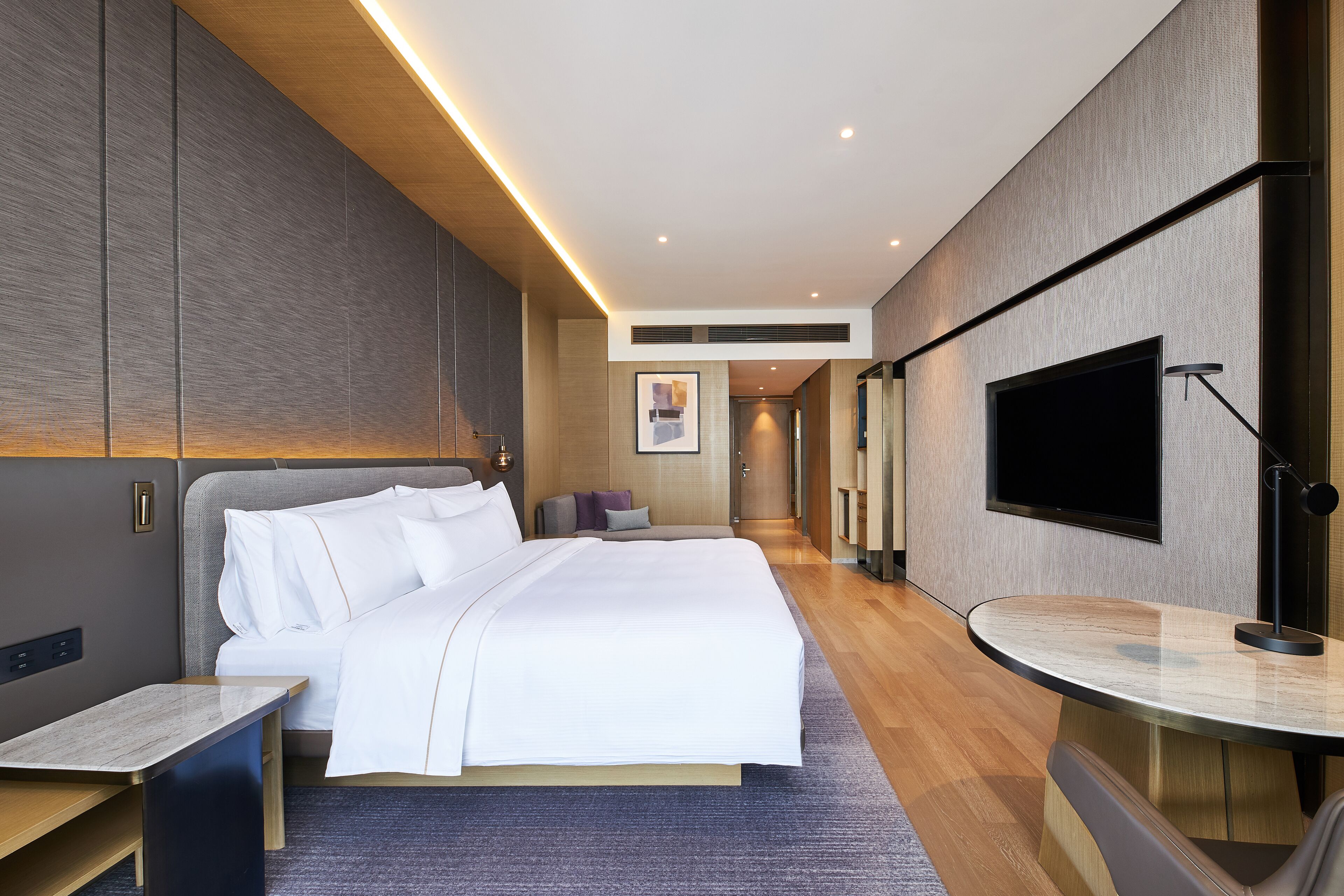 A modern hotel room with a large bed, bedside tables, a flat-screen TV, and a small seating area.