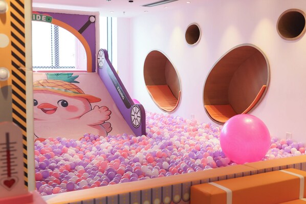 Zona de juegos infantiles con piscina de pelotas, asientos circulares y un tobogán.