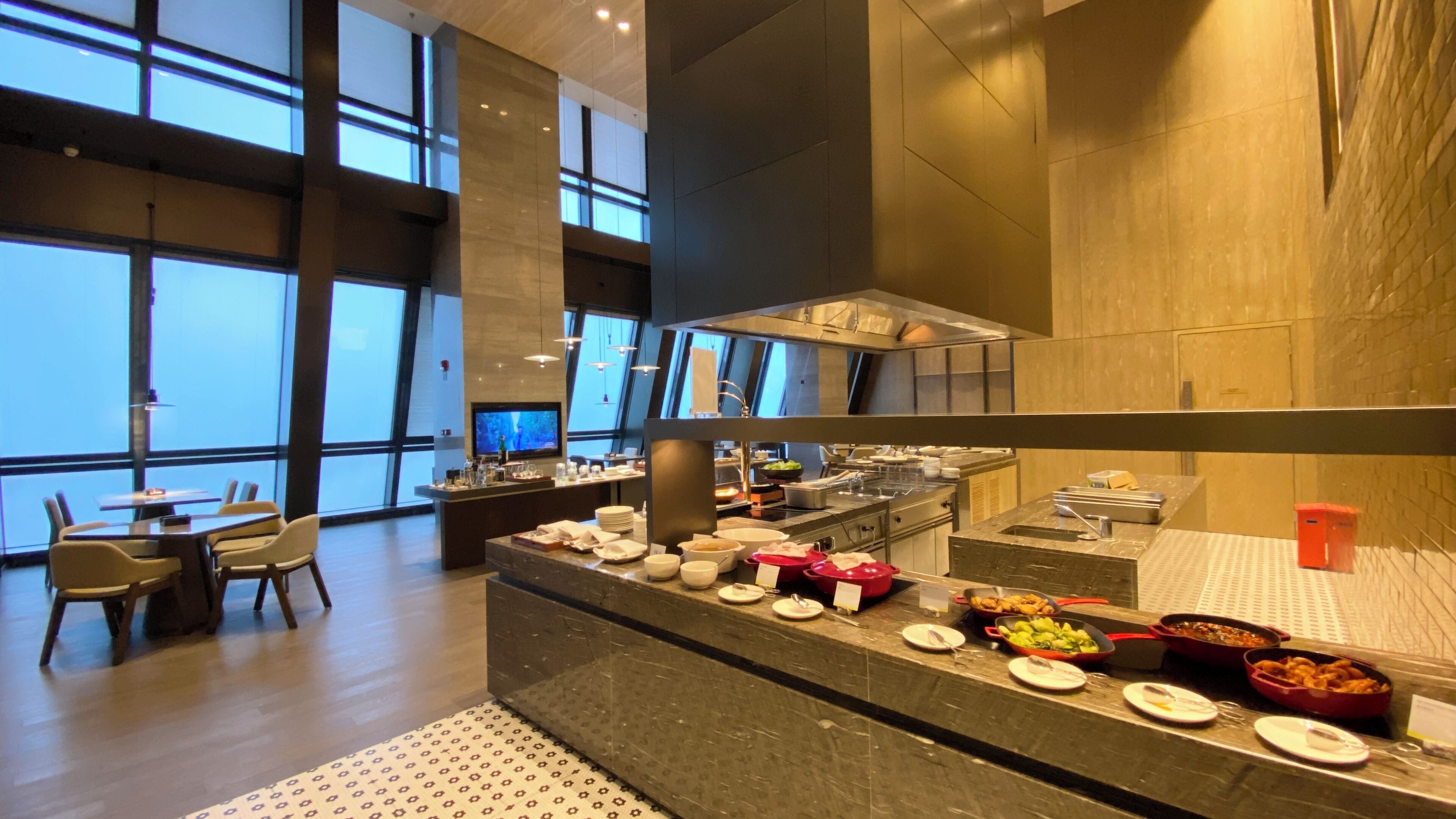 Un espace de restauration moderne dans un hôtel, avec un buffet, de grandes fenêtres et un mobilier contemporain.
