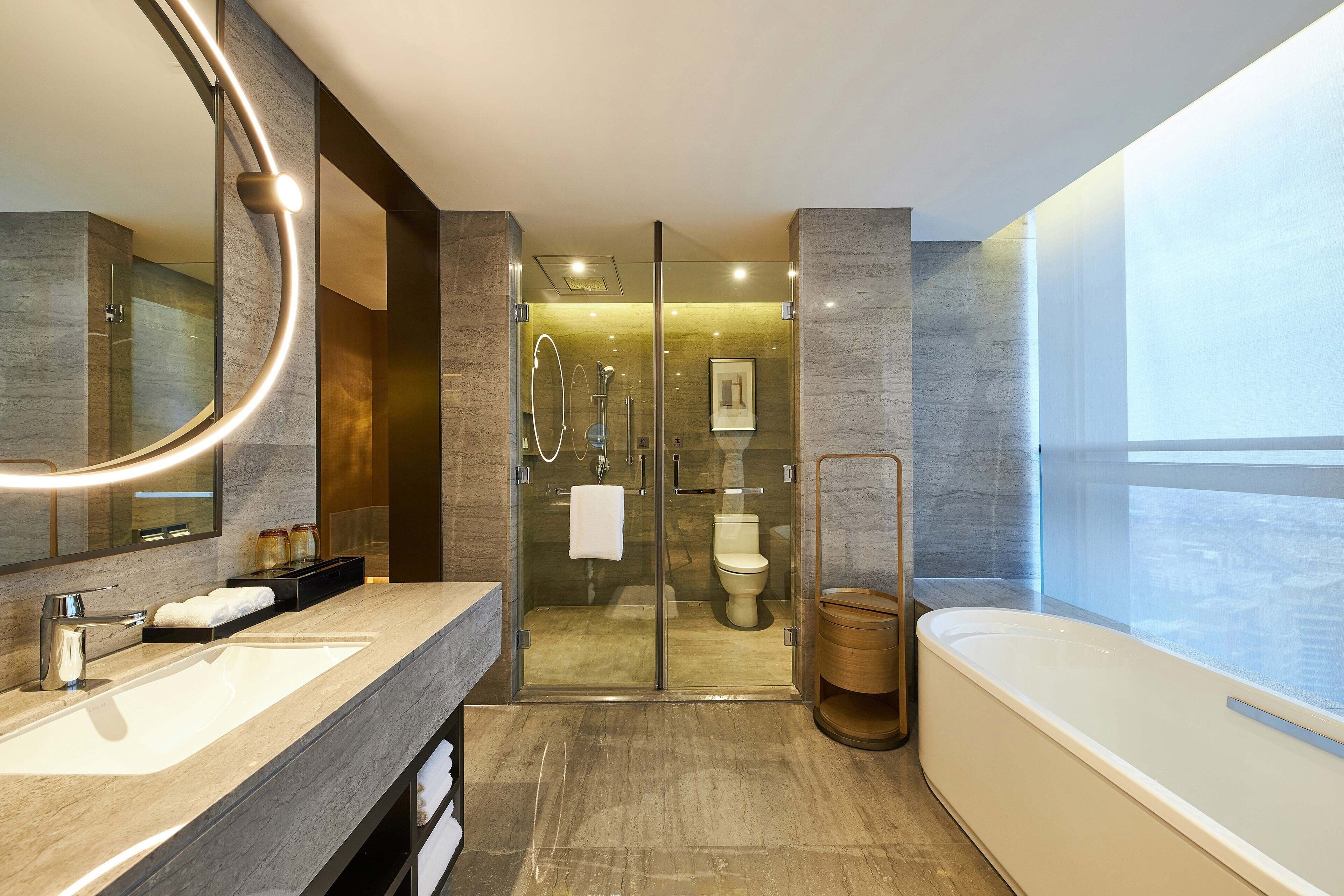A modern bathroom with a large mirror, a bathtub, a shower area, and a toilet.