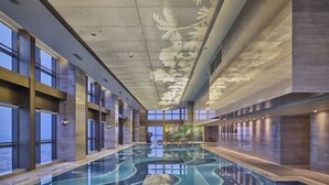 Une vaste piscine intérieure à l’eau d’un bleu limpide, entourée de hauts plafonds et de grandes fenêtres.