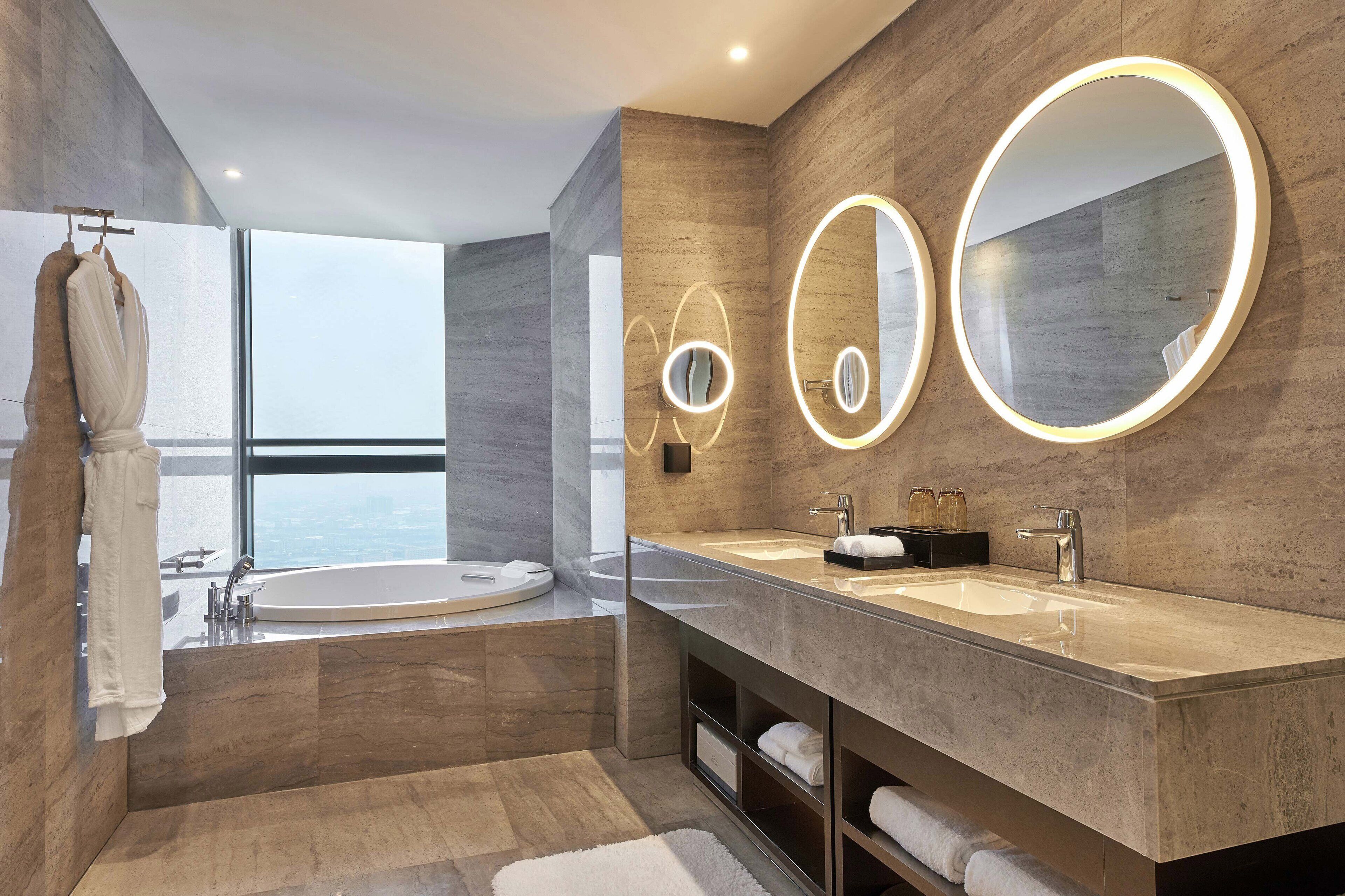 Ein modernes Badezimmer mit einer großen Badewanne, zwei Waschbecken und einem großen Spiegel mit beleuchteten Rahmen.