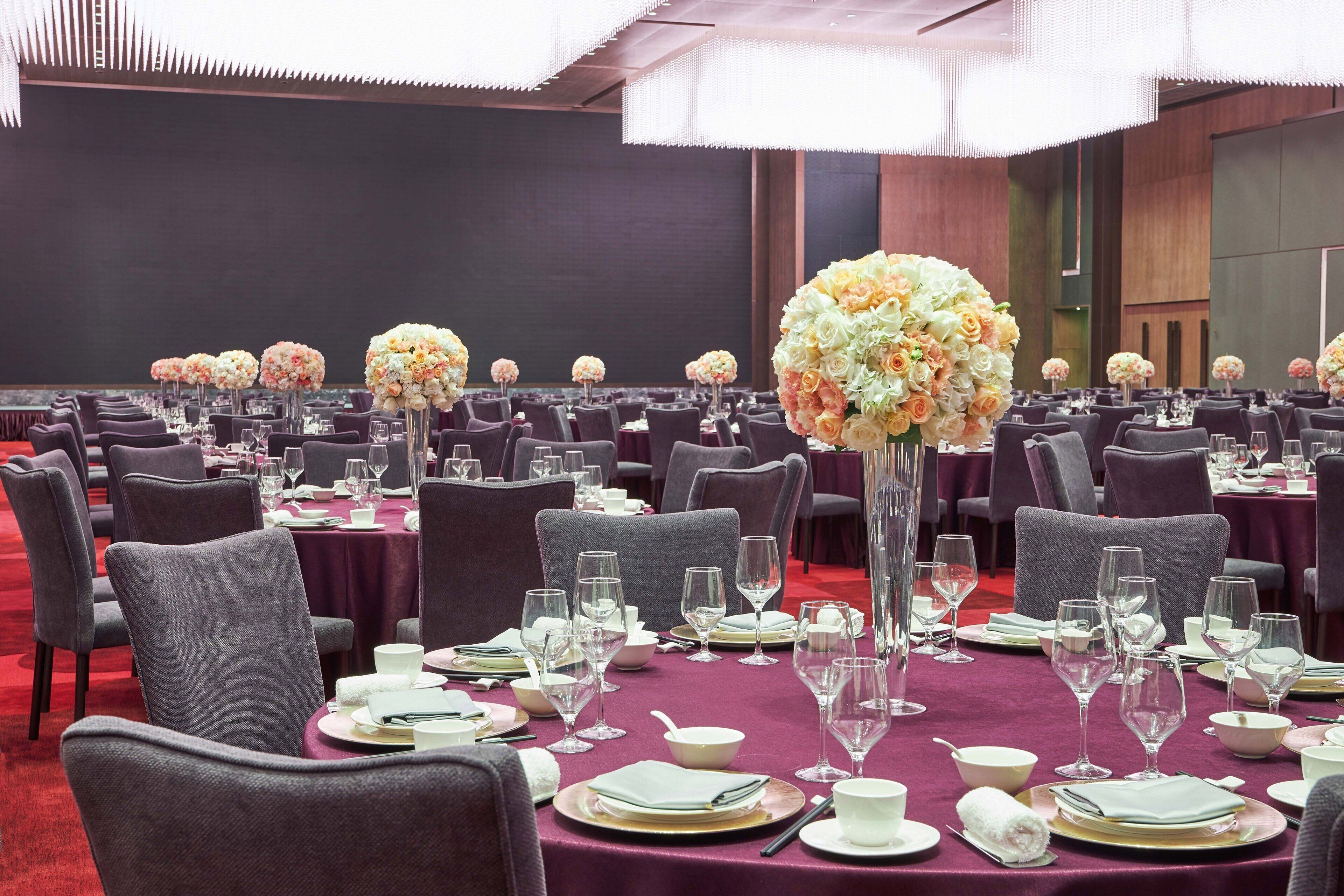 Un salón de banquetes con mesas redondas dispuestas para comer, cada una con un centro de mesa floral.