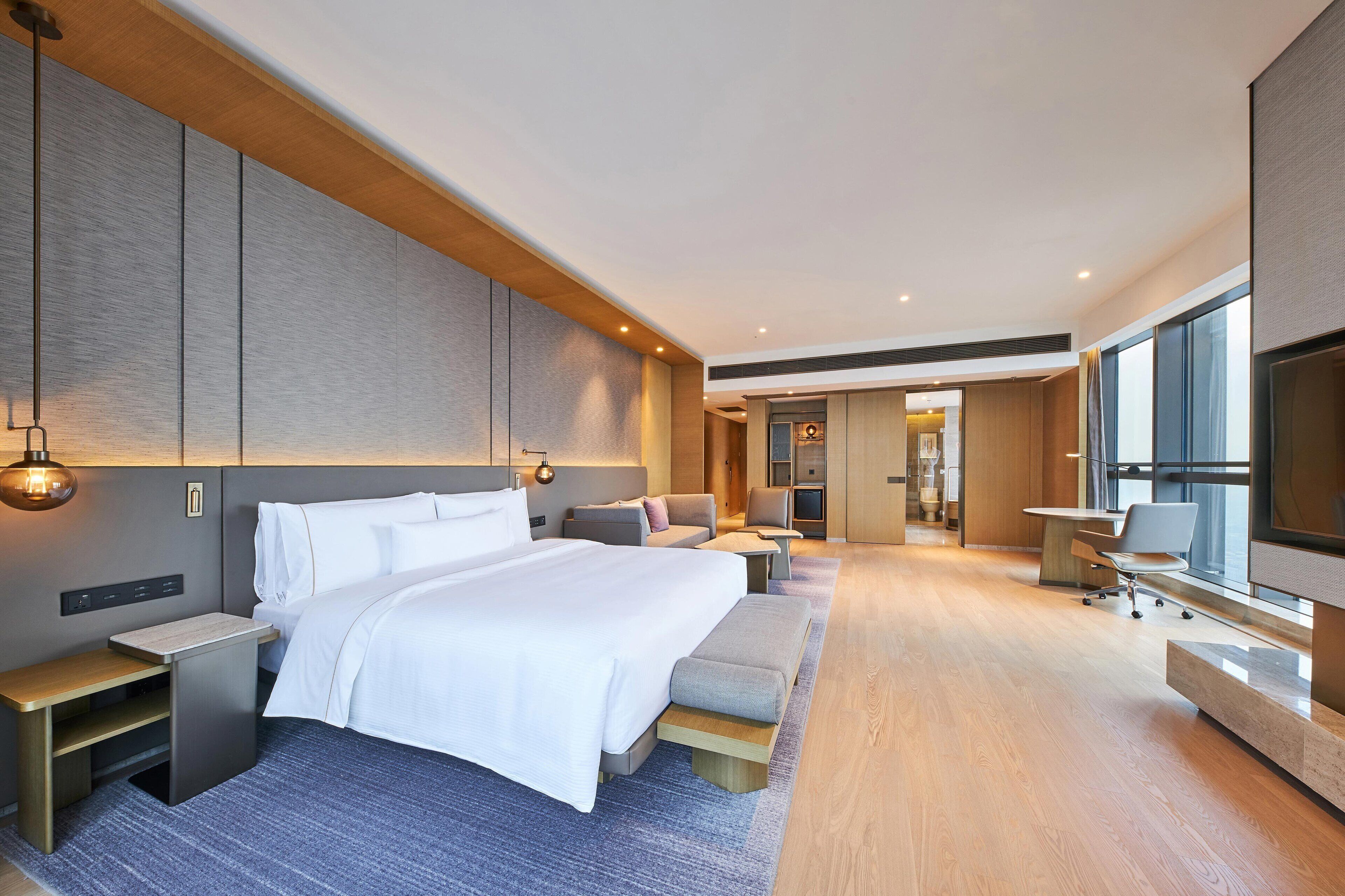 A modern hotel room with a large bed, bedside tables, a seating area, and a TV.