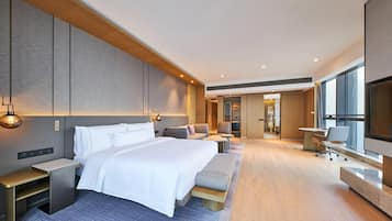 A modern hotel room with a large bed, bedside tables, a seating area, and a TV.