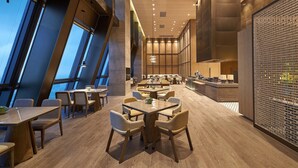 Un espace de restauration moderne avec des tables et des chaises en bois, de grandes fenêtres et un mur de briques agrémenté d’un paravent décoratif.