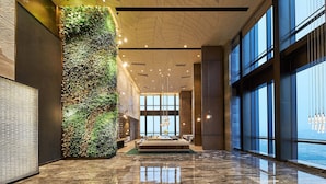 Eine großzügige Lobby mit hoher Decke, großen Fenstern, einer zentralen Sitzecke und einer vertikalen Grünwand.