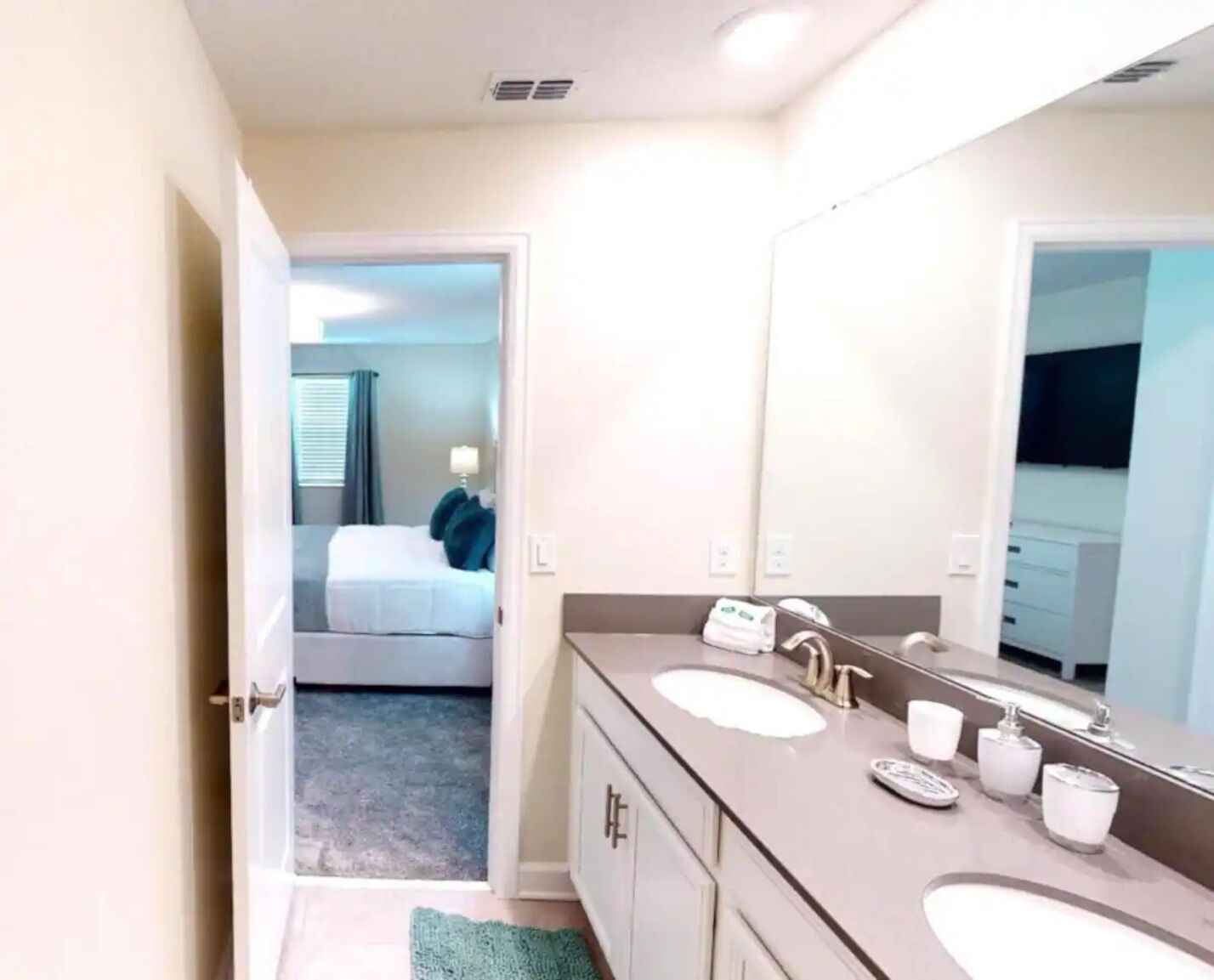 A hotel bathroom with two sinks, a large mirror, and a door leading to a bedroom.