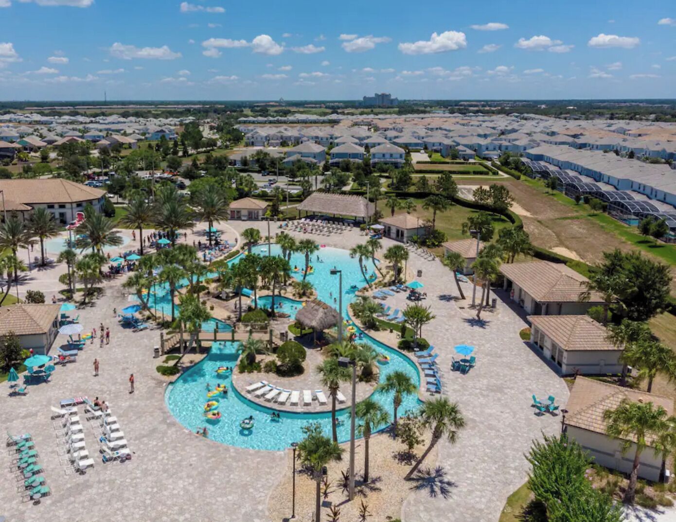 A resort with a central swimming pool, sun loungers, and palm trees.