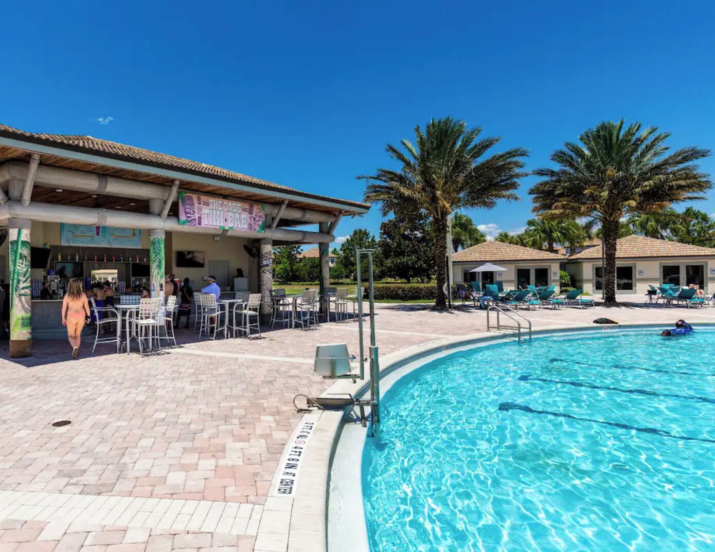 A poolside area with a bar, lounge chairs, and palm trees.