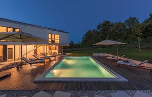 Une maison moderne dotée d’une piscine, de chaises longues et de parasols.