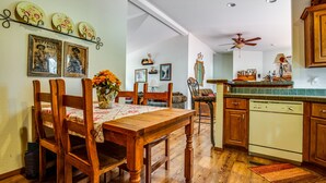 A dining area with a wooden table and chairs, a vase of flowers, and a kitchen with wooden cabinets and a dishwasher.
