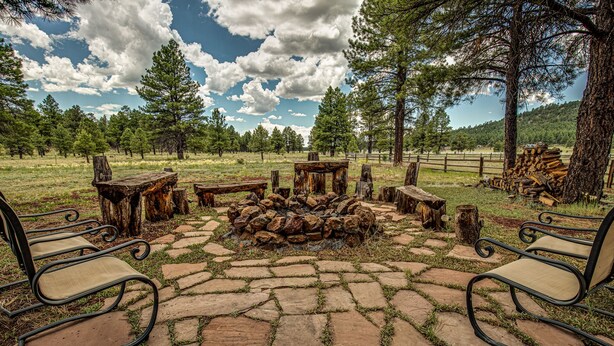 A rustic outdoor seating area with stone flooring, wooden benches, and a central fire pit.