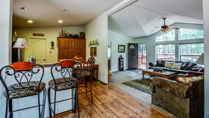 A spacious living room with a large window, a ceiling fan, and a dining area with a wooden cabinet and chairs.