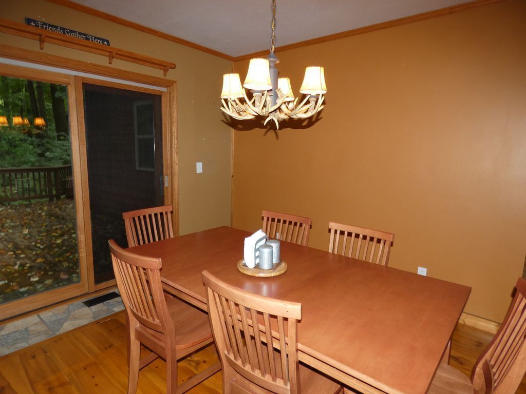 A dining area with a large wooden table and six chairs, a chandelier, and a sliding glass door leading to an outdoor area.