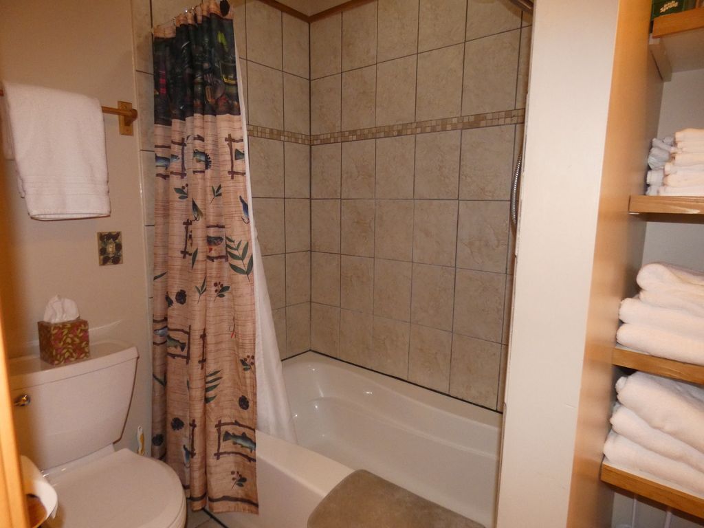 A bathroom with a bathtub, shower curtain, toilet, and a shelf with towels.