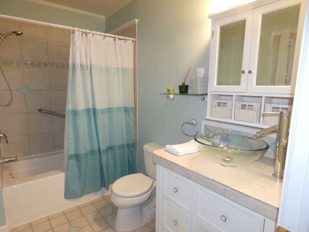 A bathroom with a shower, toilet, and a glass sink with a white cabinet above.