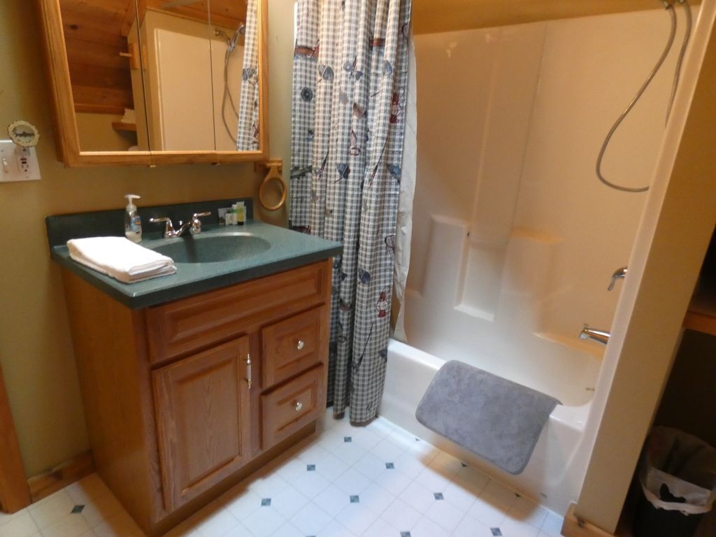 A bathroom with a wooden vanity, a sink, a mirror, a shower curtain, and a bathtub.