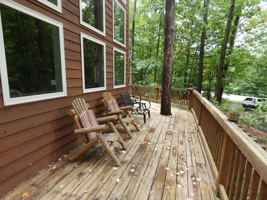 A wooden deck with a railing, two rocking chairs, and a table.