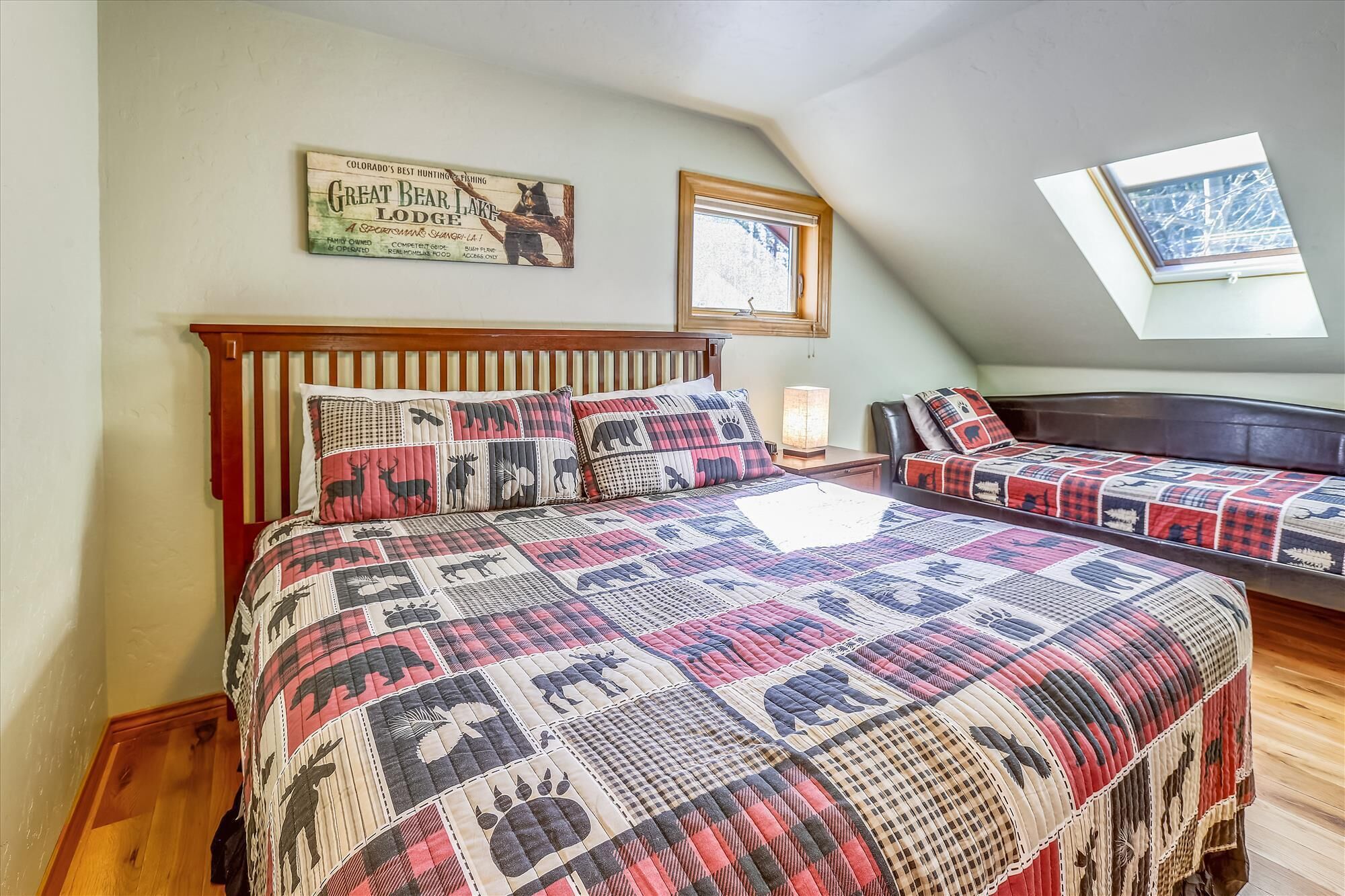 A bedroom with a wooden bed, a quilt with animal prints, a window, and a sign on the wall.
