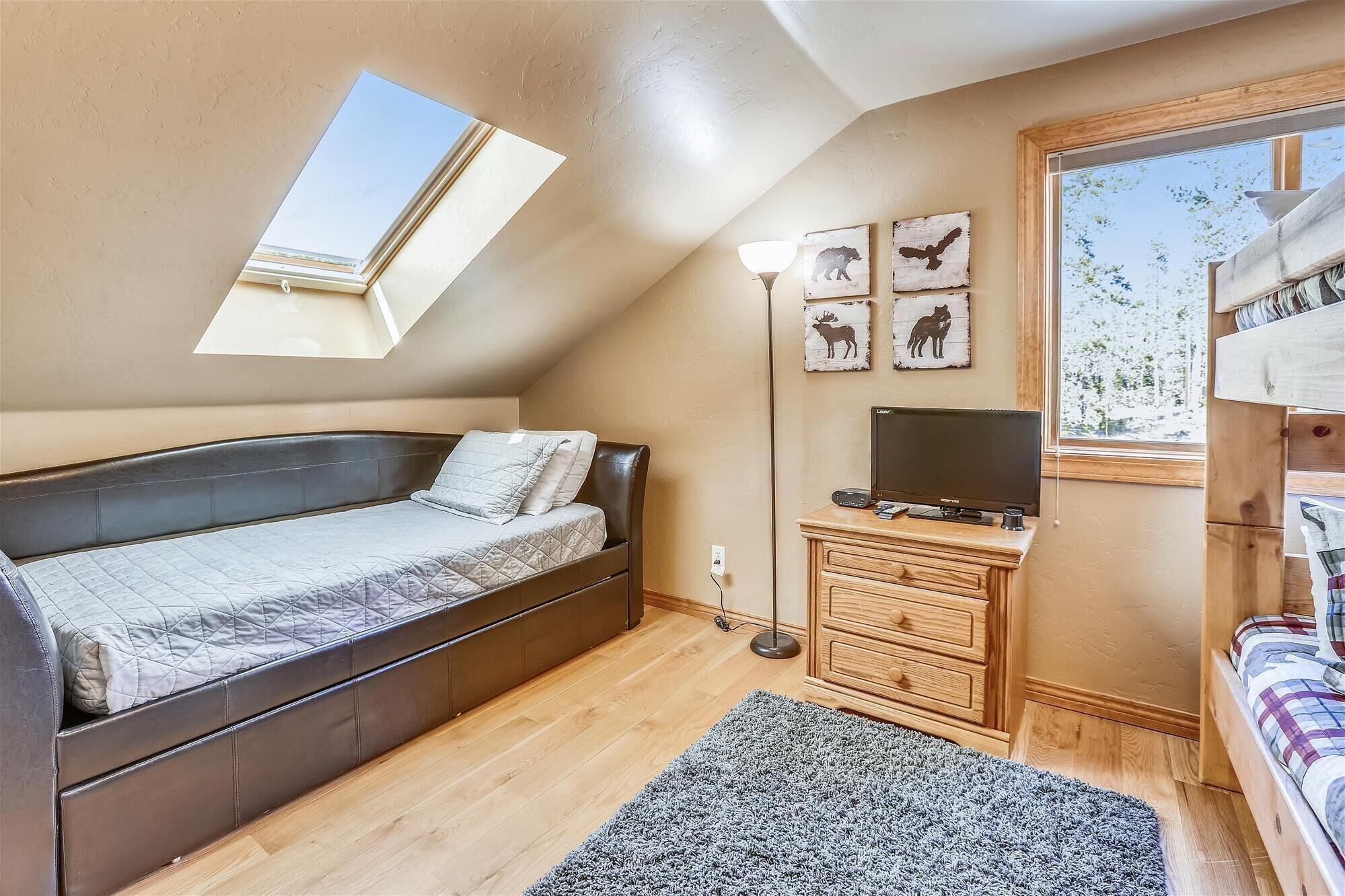 A bedroom with a loft bed, a skylight, a desk with a computer, and wall art.