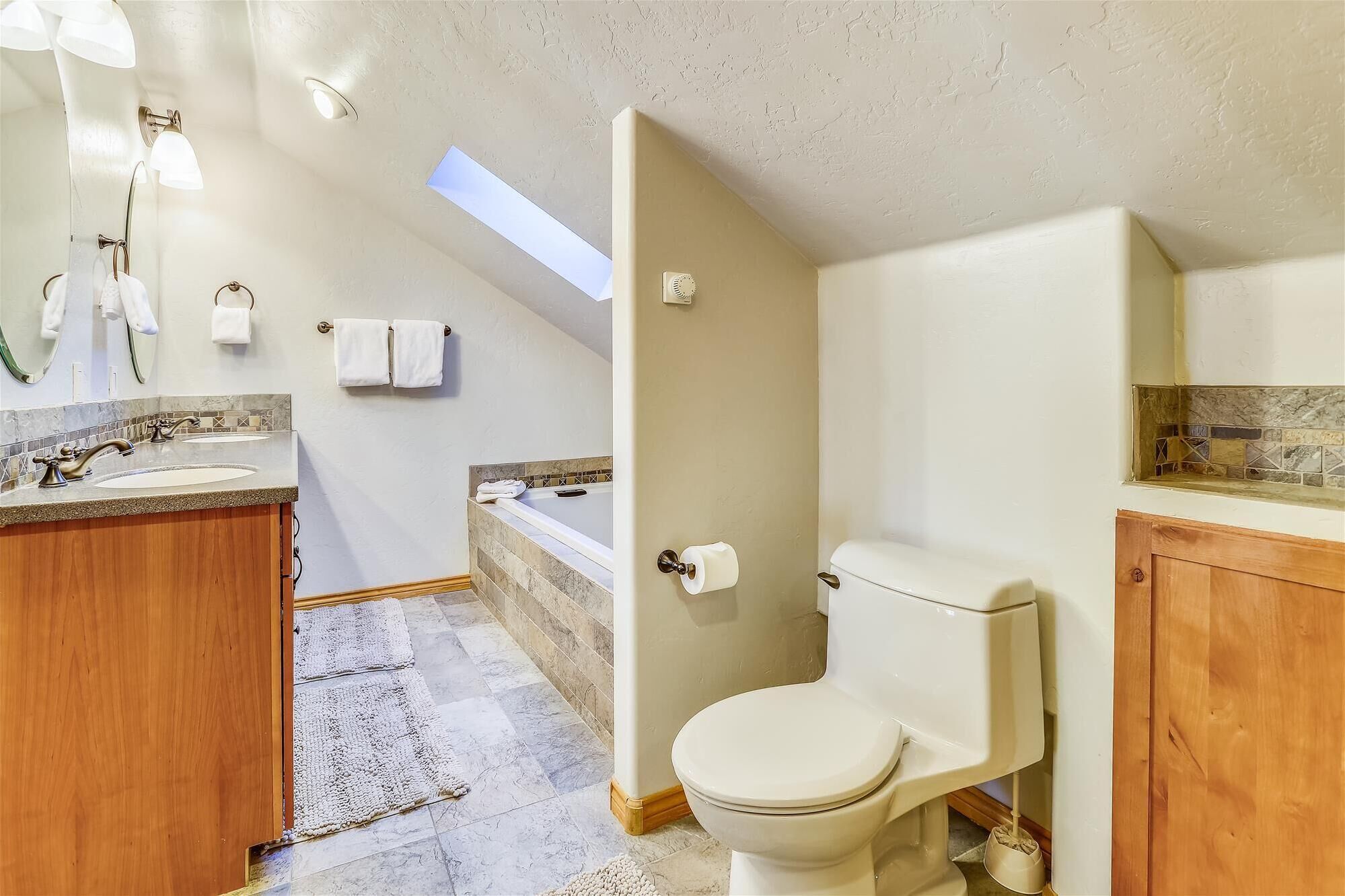 Une salle de bain avec une baignoire, des toilettes et un lavabo. Il y a une lucarne au-dessus de la baignoire et un porte-serviettes avec des serviettes.
