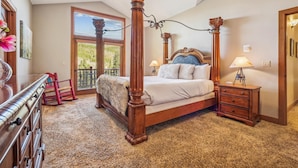 A four-poster bed with a wooden headboard, a nightstand with a lamp, a dresser with drawers, and a window with blinds. - Spacious Breck Ski Home, Multiple Fireplaces, Gondola 2.1mi, Sleeps 10 (Breckenridge)