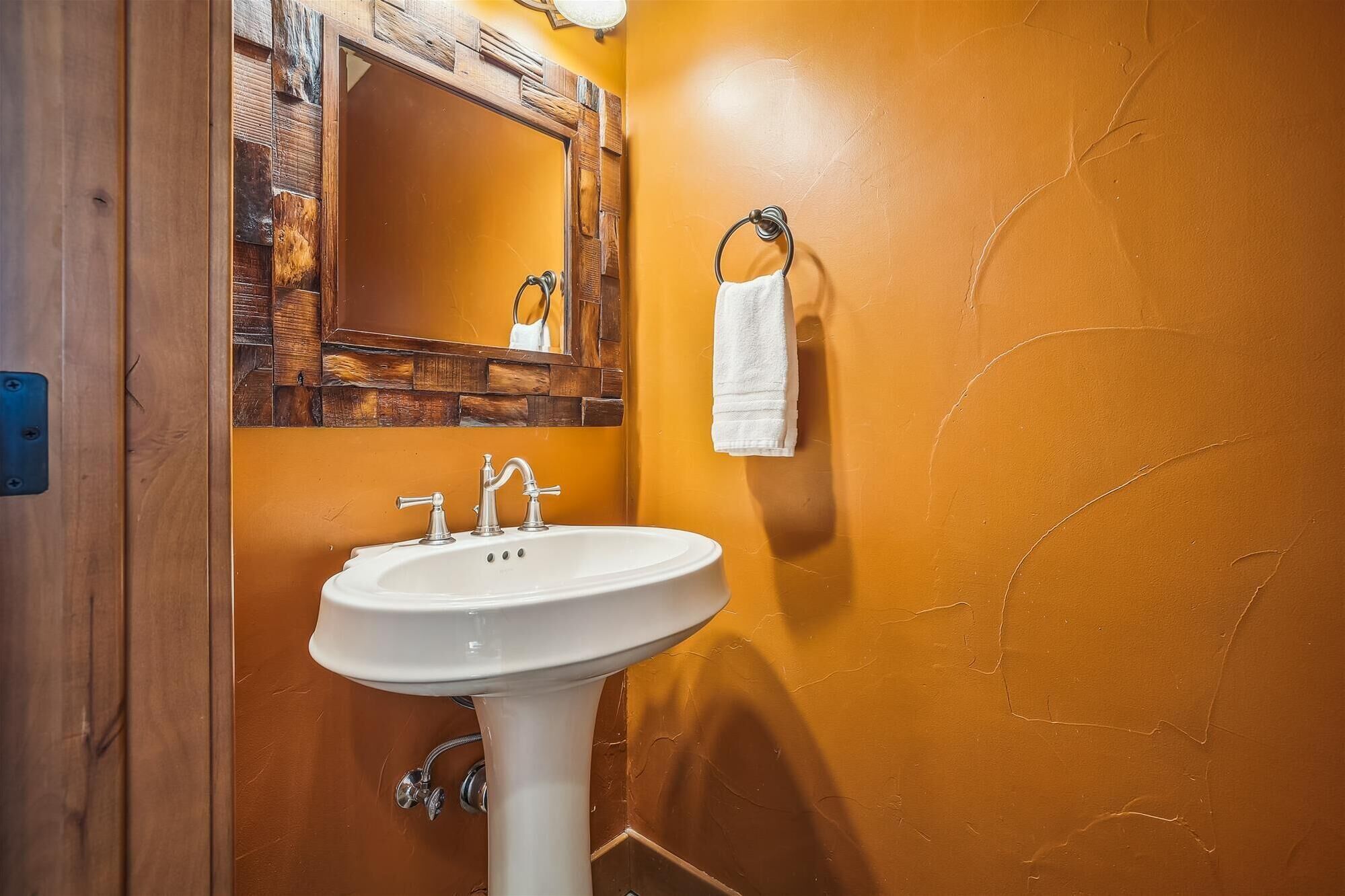 Un baño con lavamanos blanco, paneles de madera en la pared y un espejo.