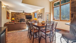 A spacious living area with a stone fireplace, a flat-screen TV, and a dining table with chairs. - Spacious Breck Ski Home, Multiple Fireplaces, Gondola 2.1mi, Sleeps 10 (Breckenridge)