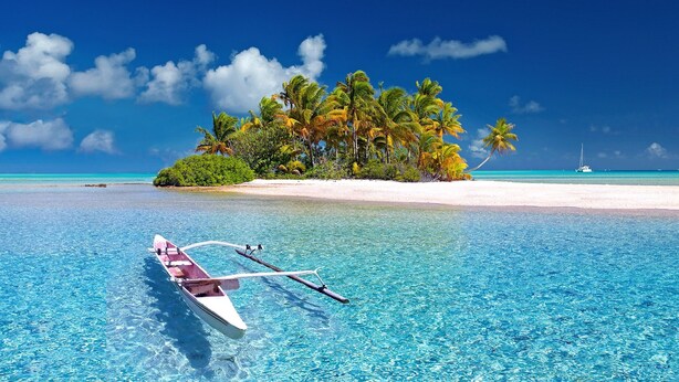 A clear blue sea with a boat in the foreground, a sandy beach, and a small island with palm trees. - San Blas Private Sailboat - Island Hopping (Narganá)