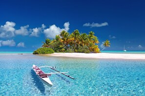 A clear blue sea with a boat in the foreground, a sandy beach, and a small island with palm trees. - San Blas Private Sailboat - Island Hopping (Narganá)