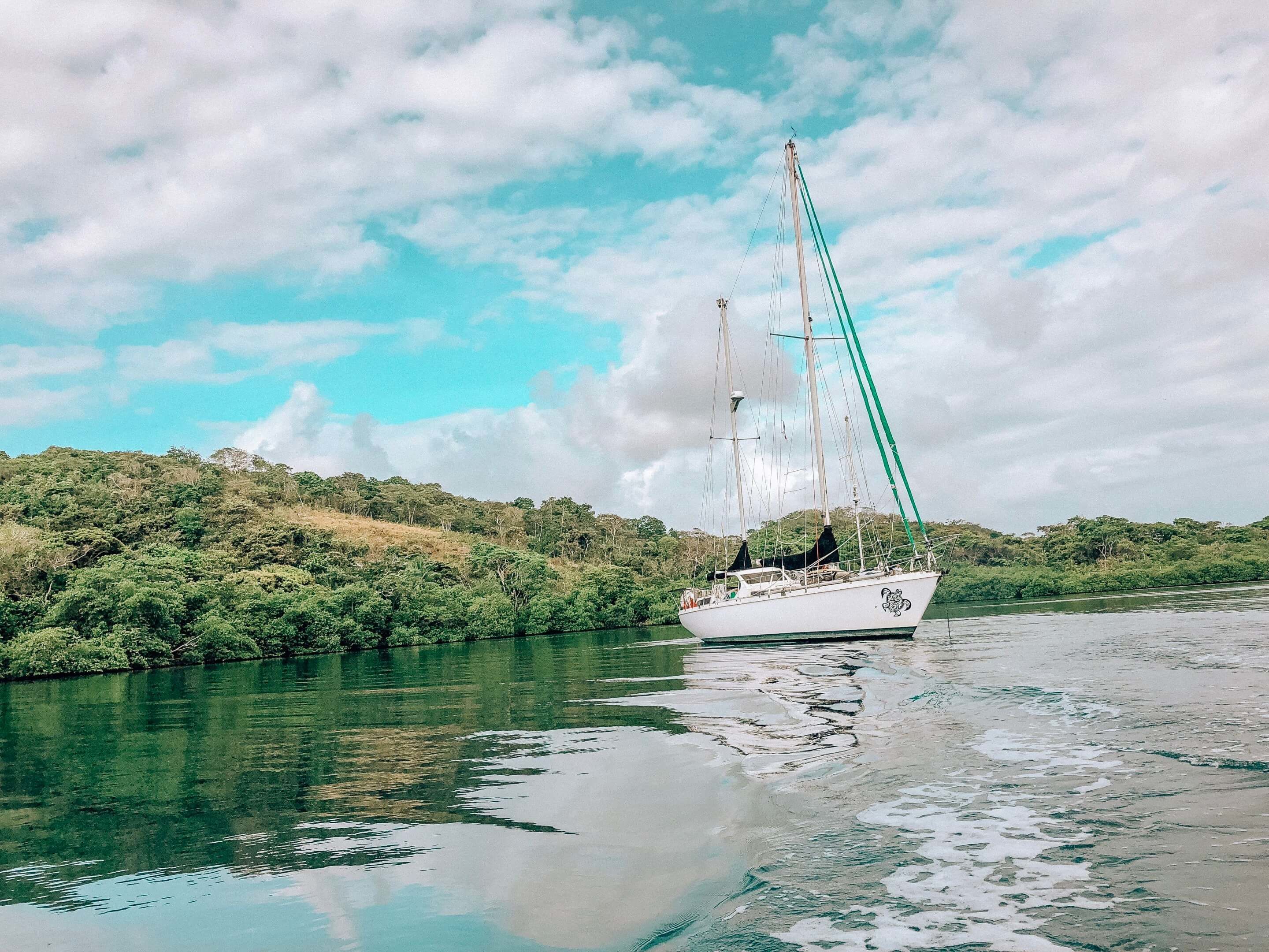 Un voilier sur une rivière paisible, bordée d’une végétation luxuriante.