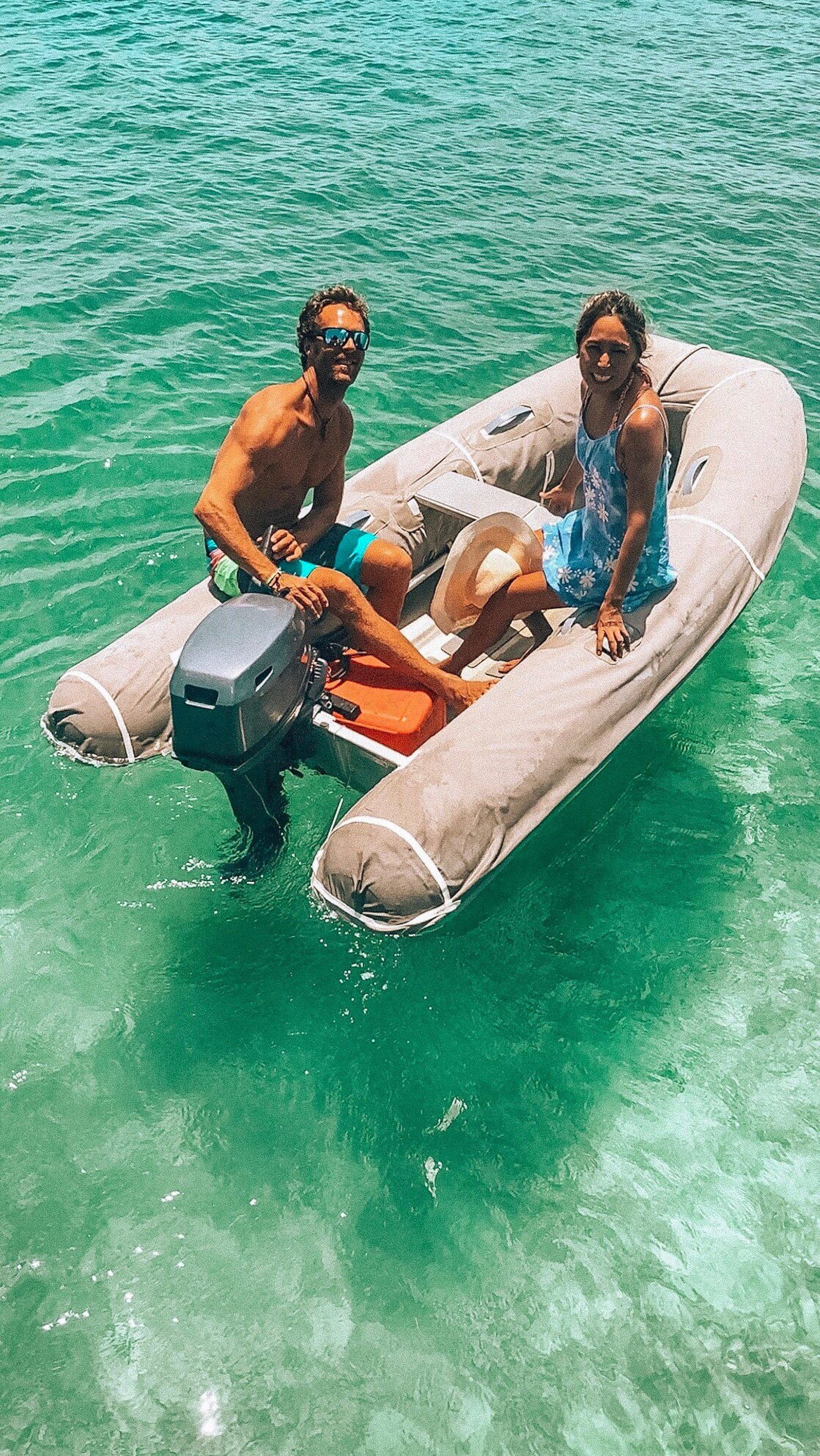 A small inflatable boat with two people and a dog on a clear turquoise sea.