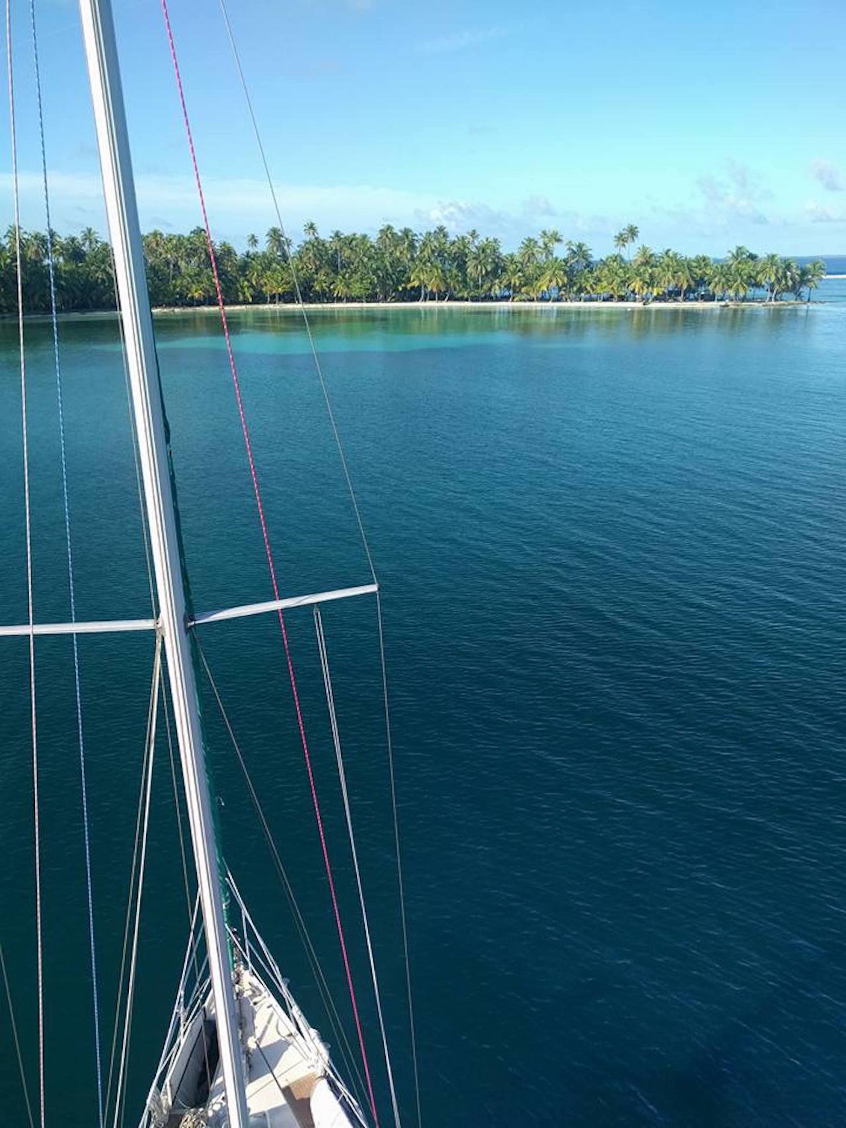 Un voilier sur des eaux calmes, avec une vue dégagée sur une île tropicale au loin.