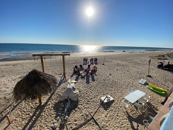 Ein Strand mit einer strohgedeckten Konstruktion, einem Tisch mit Stühlen und einem Rettungsschwimmerstand.