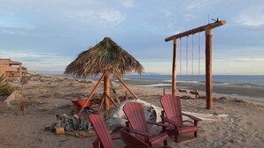 Eine Strandlandschaft mit Holzstühlen, einer Reetdachkonstruktion und einer Schaukel.