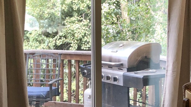 Une porte-fenêtre coulissante donnant sur une terrasse équipée d’un barbecue et de mobilier d’extérieur.