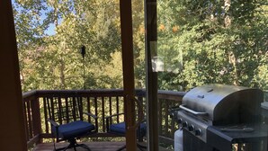 Une terrasse en bois avec un barbecue et deux chaises bleues.