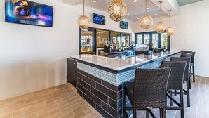 A bar area with a counter, bar stools, hanging light fixtures, and a television mounted on the wall. - Fresh Heaven Pool Home by AV Dreams (Kissimmee)
