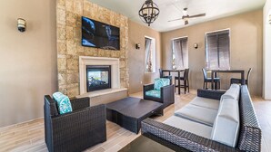 A modern outdoor living area with wicker furniture, a stone wall, a flat-screen TV, and a ceiling fan. - Fresh Heaven Pool Home by AV Dreams (Kissimmee)