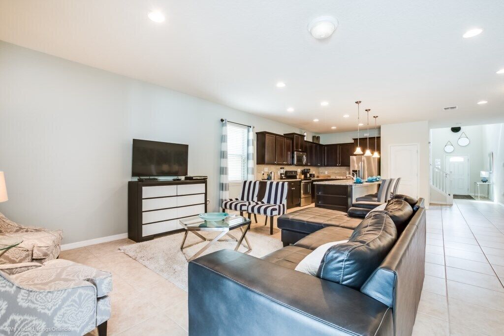 A modern living room with a sofa, a TV, and a dining area with a kitchen in the background.