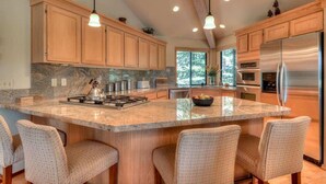 A spacious kitchen with wooden cabinets, a large island with bar stools, stainless steel appliances, and a view of the outdoors through the windows. - Luxurious home on the golf course (Sunriver)