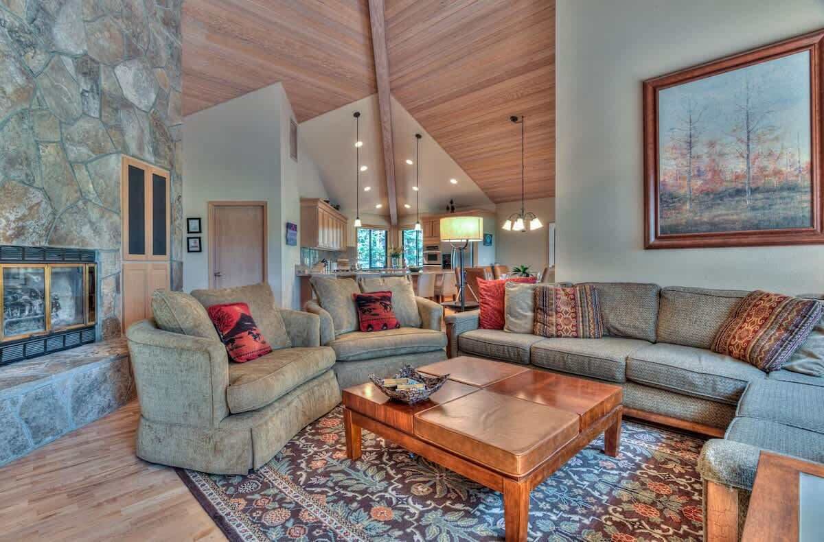 A spacious living room with a stone wall, wooden ceiling beams, and a large painting.