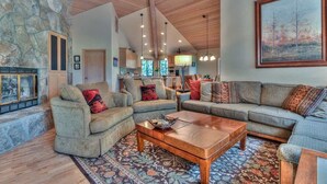 A spacious living room with a stone wall, wooden ceiling beams, and a large painting. - Luxurious home on the golf course (Sunriver)